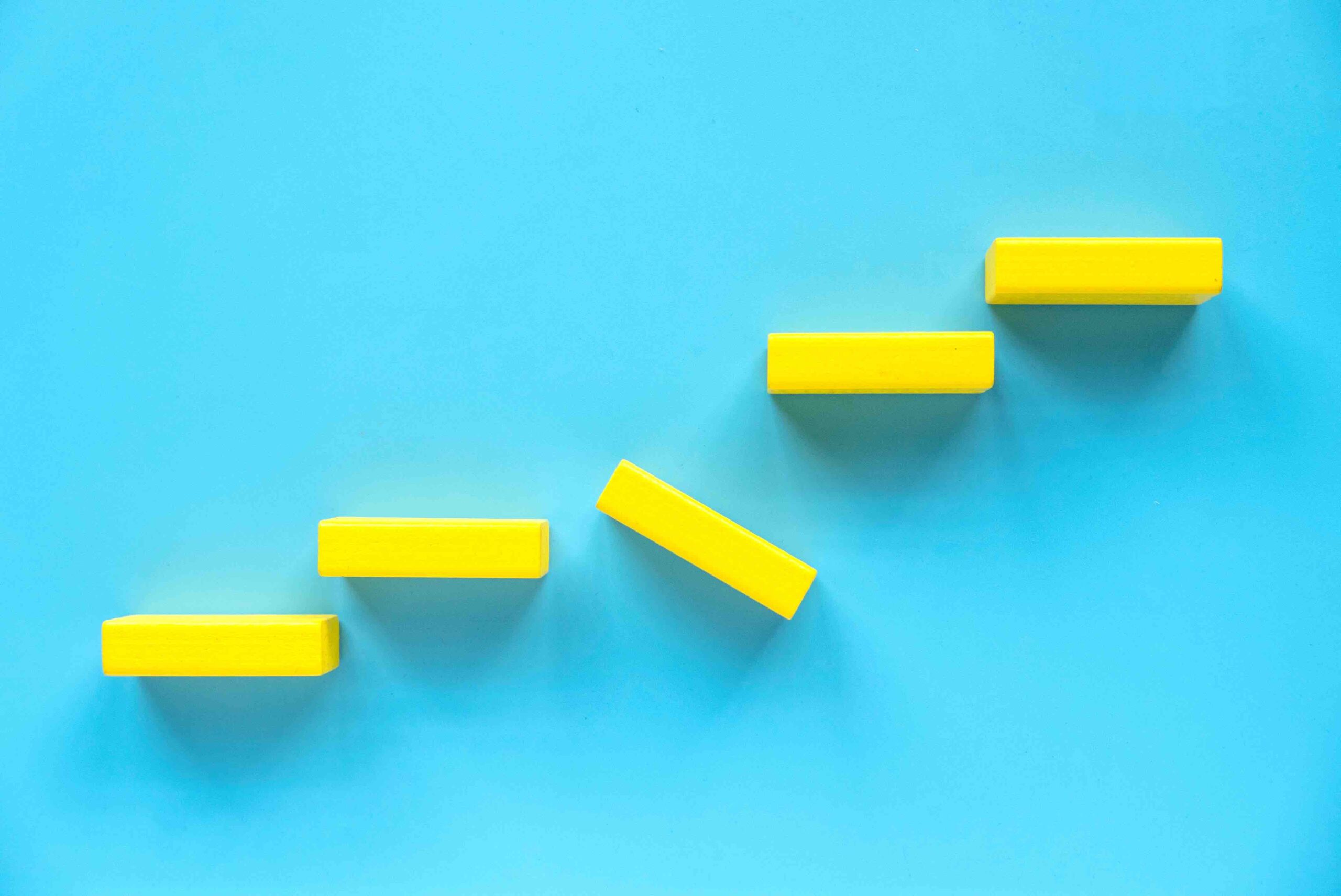 Yellow blocks along a wall with the block in the middle of kilter. Meant to show a stumbling block along the path to success.