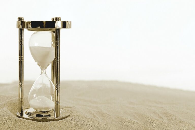 photo of a large hourglass sitting on sand. White background
