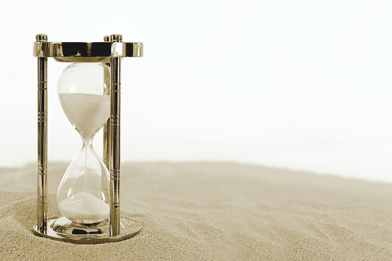 photo of a large hourglass sitting on sand. White background