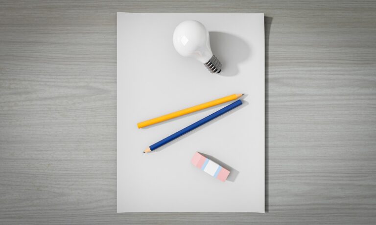 photograph of a blank piece of paper on a grey table. Light bulb, pencil, and eraser are placed on the blank piece of paper.