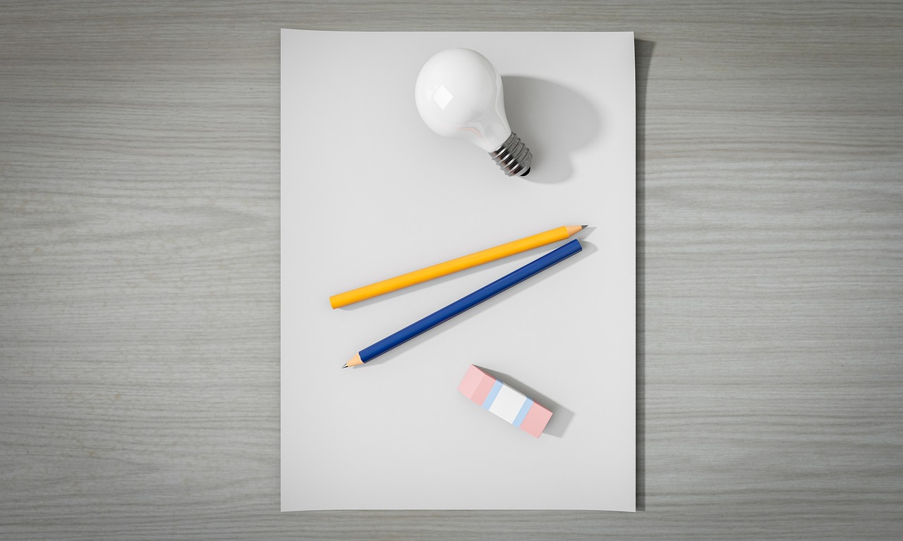 photograph of a blank piece of paper on a grey table. Light bulb, pencil, and eraser are placed on the blank piece of paper.