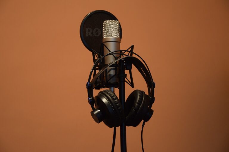 photo of a RODE microphone, windscreen/pop filer on a stand with a pair of black headphones. Room wall is a soft orange.