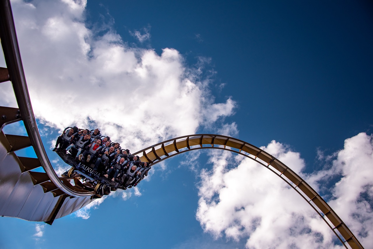 Blue sky, puffy white clouds, roller coaster with a car full of people. This photo is from Pasi Mämmelä from Pixabay Link: https://pixabay.com/photos/roller-coaster-liseberg-sweden-7255670/